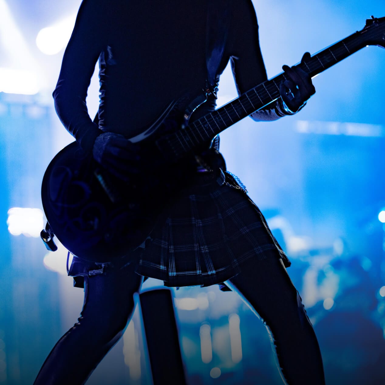 A guitarist is silhouetted against the bright lights of a concert stage.
