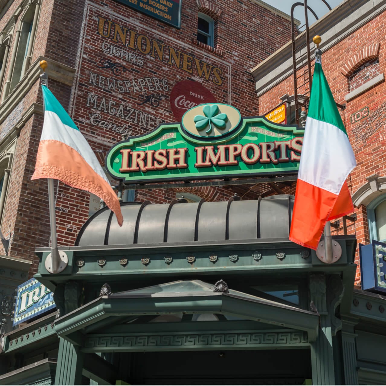 The outdoor sign for Rosie's Irish Imports in Universal Studios Orlando is flanked by two orange, white, and green Irish flags.