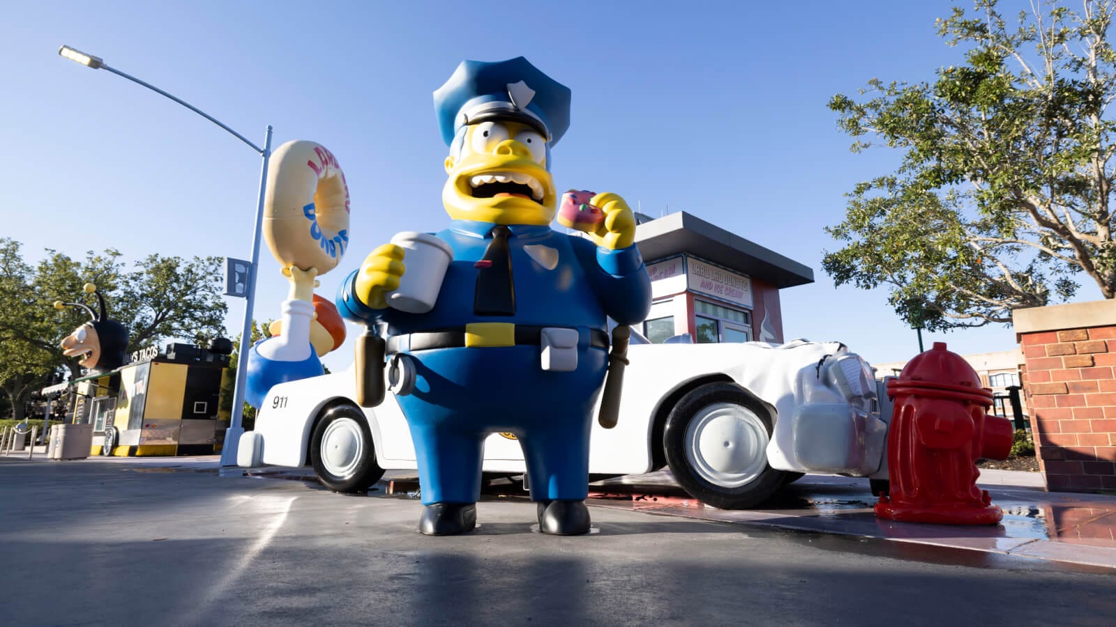 A large statue of Chief Wiggum holding a coffee and donut in front of a car crashed into a red fire hydrant.