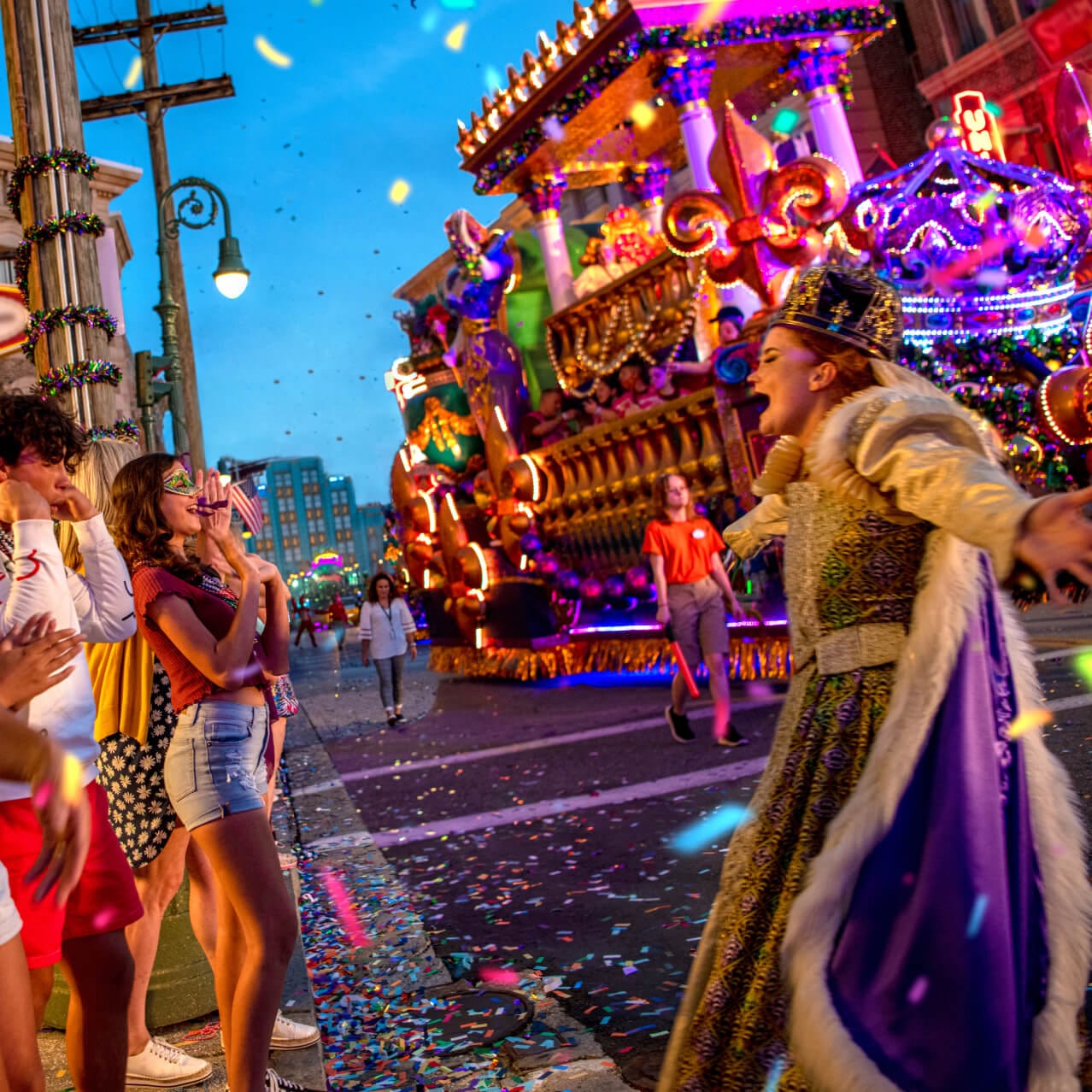 Guests throw beads from atop a parade float at Universal Mardi Gras: International Flavors of Carnaval while a performer dressed like a queen shouts to the crowd.