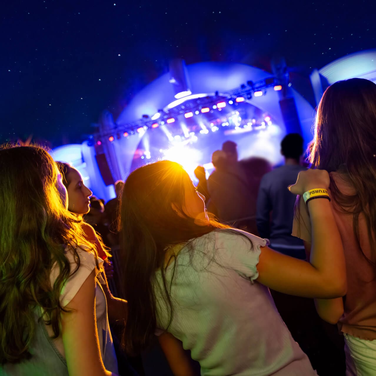 Three friends facing the stage as they watch a performance during Universal Mardi Gras.