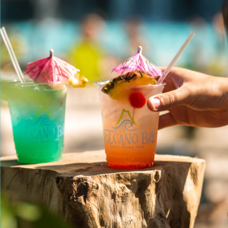 A hand reaching for tropical drinks with mini umbrellas resting on a table.