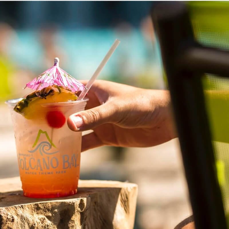 Image of tropical drinks resting on low post with hand reaching in from left to grasp one.