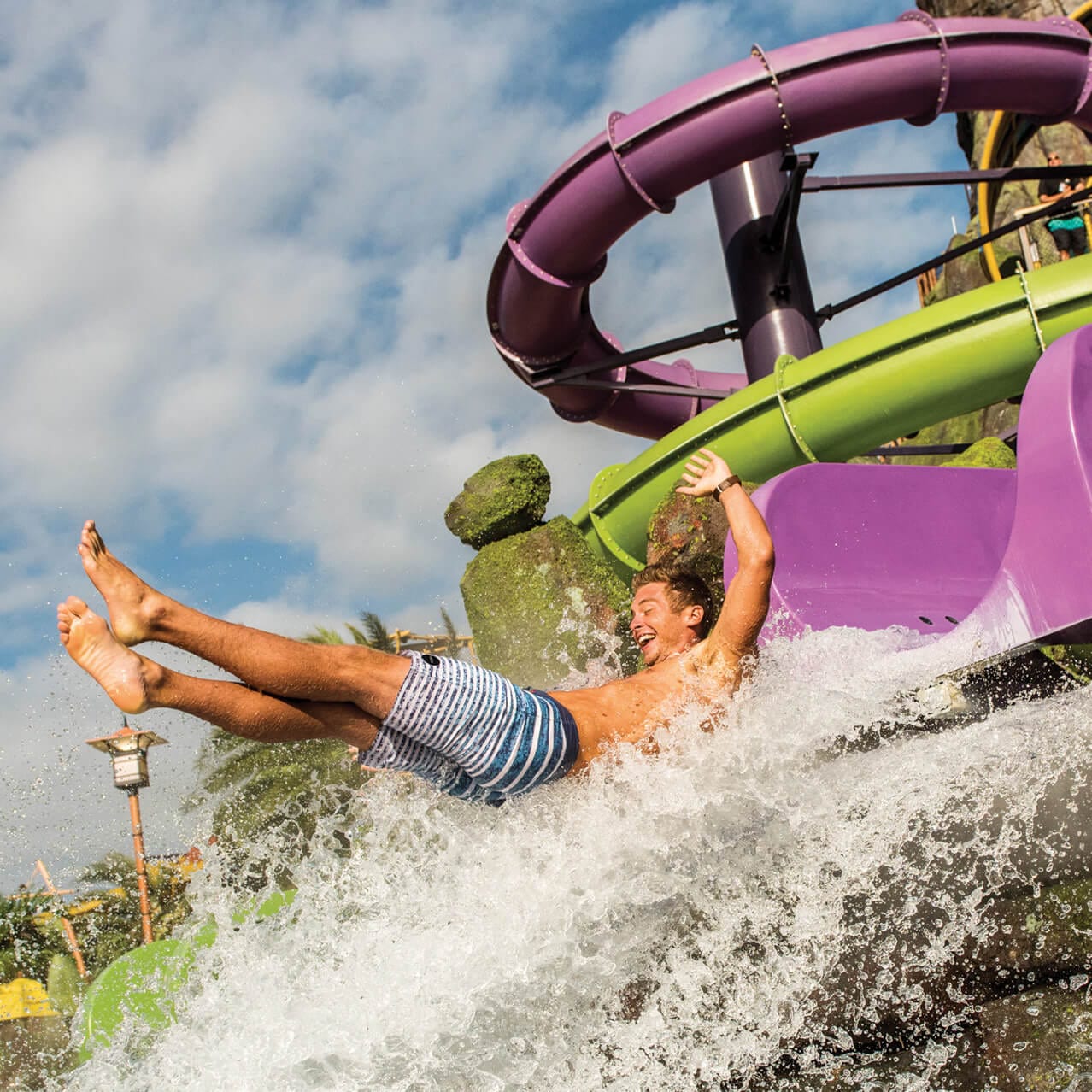 A man slides into the water on the Ohno of Ohyah & Ohno Drop Slides at Universal Volcano Bay.