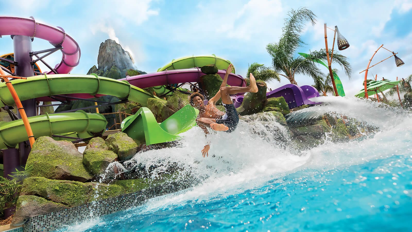 A young man slides into the water on the Ohno of Ohyah & Ohno Drop Slides at Universal Volcano Bay.