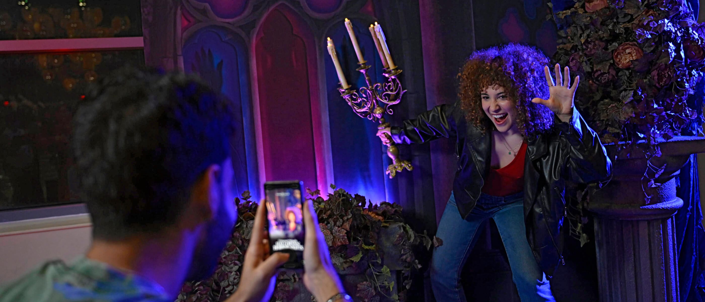 A&nbsp;guest&nbsp;posing&nbsp;with&nbsp;a&nbsp;candelabra&nbsp;in&nbsp;an&nbsp;eerie&nbsp;mansion&nbsp;backdrop&nbsp;while&nbsp;another&nbsp;takes&nbsp;their&nbsp;photo&nbsp;in&nbsp;the&nbsp;Loews&nbsp;Sapphire&nbsp;Falls&nbsp;Resort&nbsp;lobby.