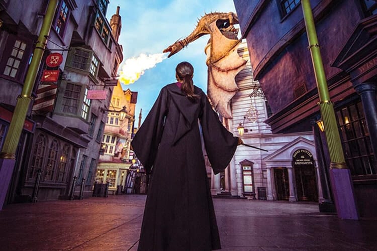 A girl wearing a wizard robes stands before a fire-breathing dragon in Diagon Alley at Universal Studios Florida.