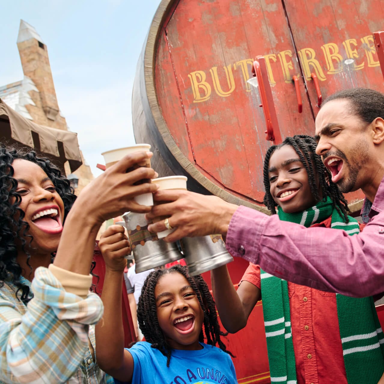 An excited family of four holding cheering as they hold up their Butterbeer in The Wizarding World of Harry Potter™.