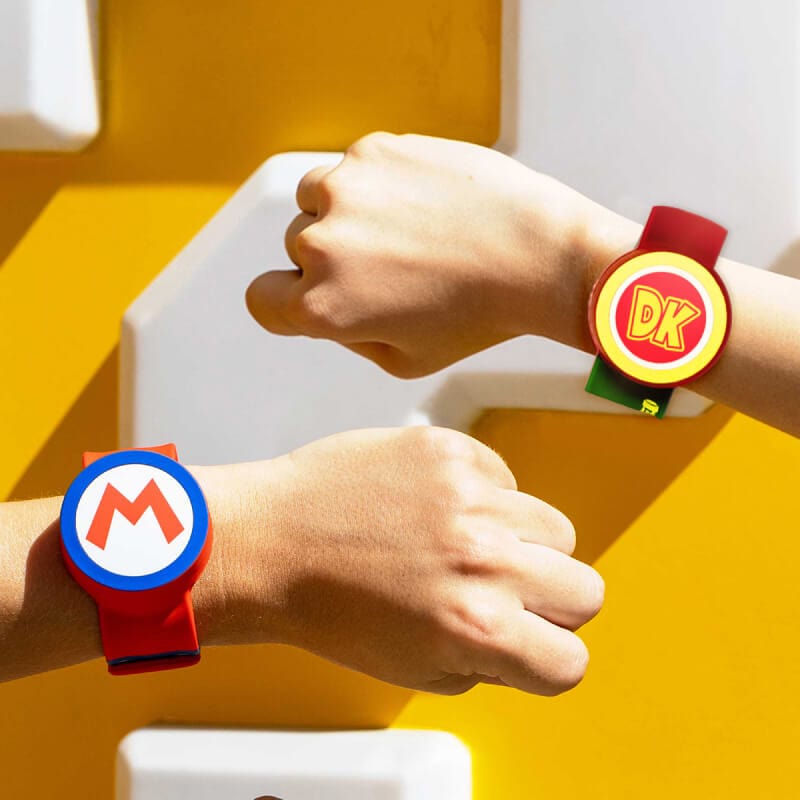 Two arms featuring a Mario™ and a Donkey Kong™- themed SUPER NINTENDO WORLD™ Power-Up Band™.