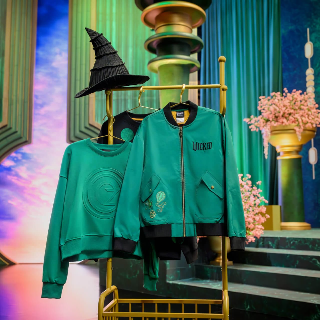 Wicked: For Good merchandise including an emerald green sweatshirt and an emerald green and black zip-up jacket.