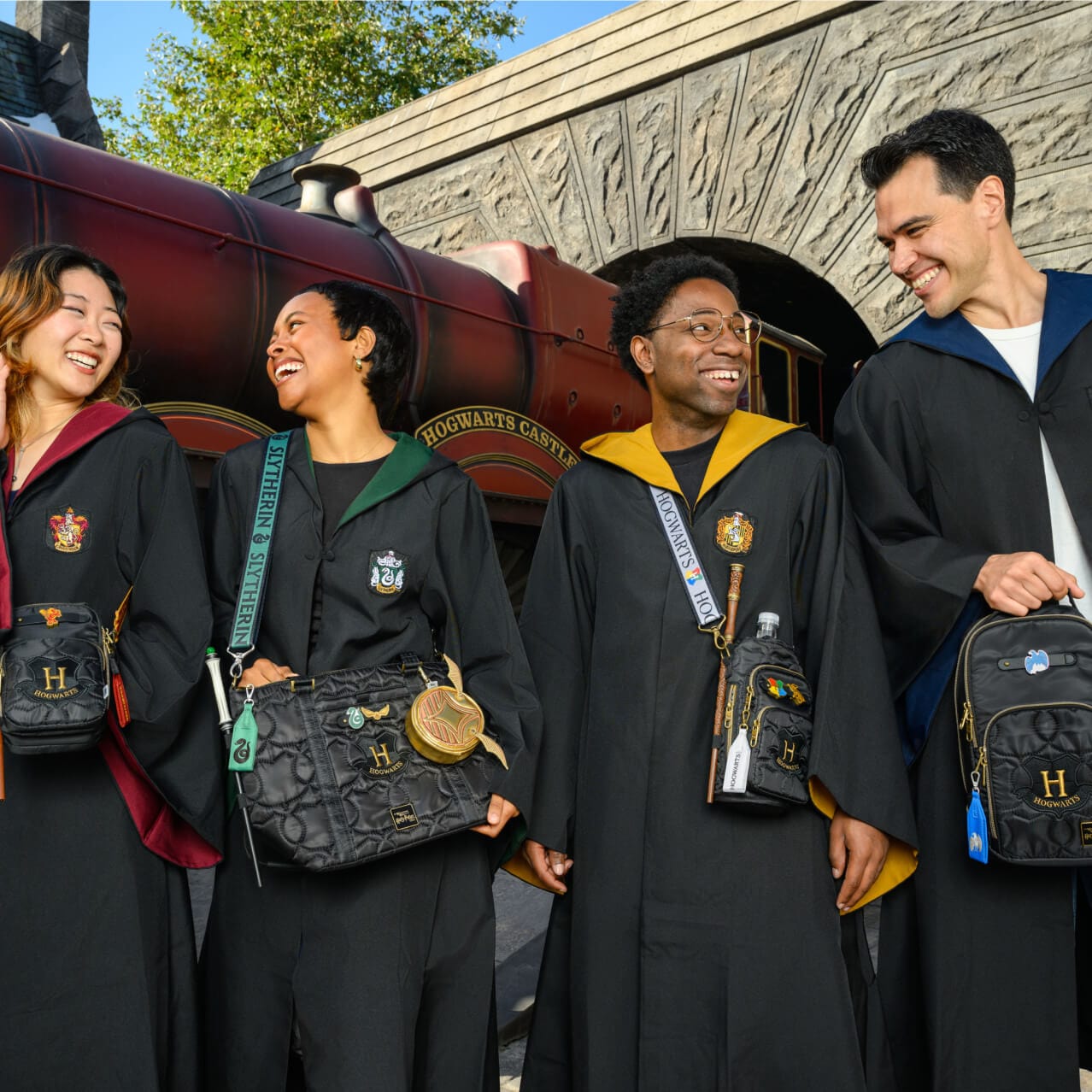 Four friends by the Hogwarts Express™ wearing robes and matching Lug Build-A-Bags representing the four Hogwarts houses.