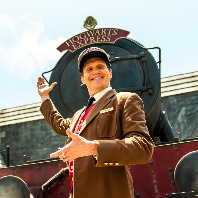 A conductor standing in front of the Hogwarts Express™ in The Wizarding World of Harry Potter™.