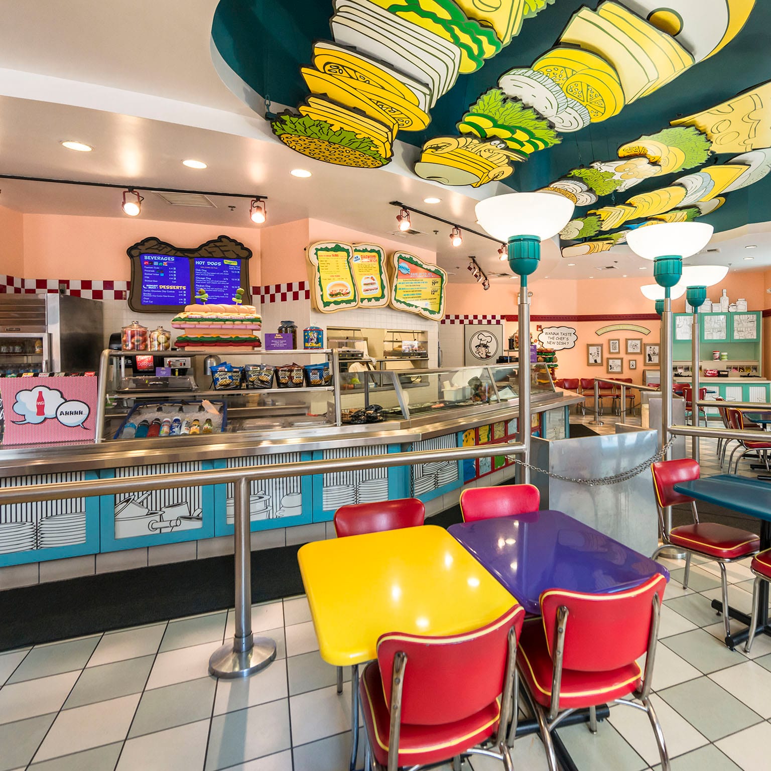 The interior of Blondie's: Home of the Dagwood, featuring colorful tables and chairs and a cartoon inspired counter where guests can order specialty sandwiches, subs, and hot dogs.