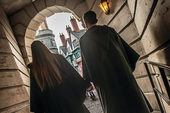 When you stay at an on site resort hotel, you can enjoy early park admission to see the Wizarding World of Harry Potter before other guests. Their backs to us, a boy and a girl in Hogwarts™ robes walk though a stone archway into The Wizarding World of Harry Potter™ - Diagon Alley™.