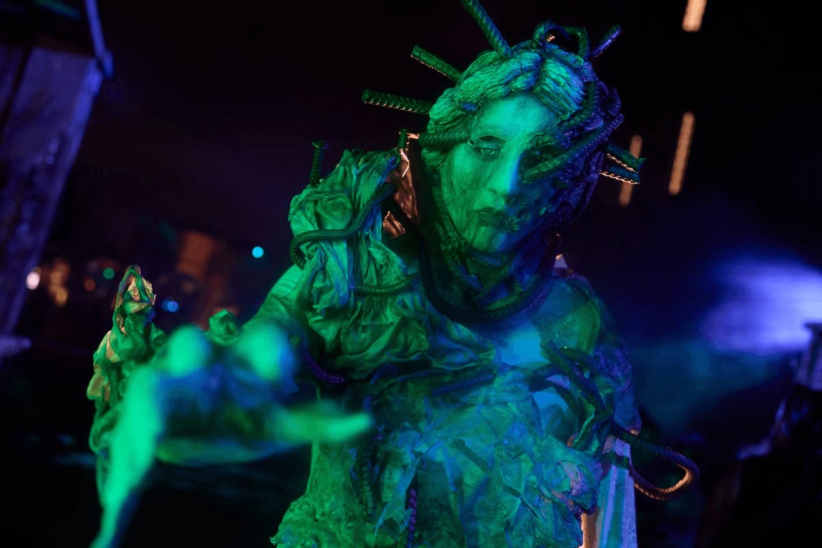 A glowing green scareactor with a head full of spikes reaching out a dripping hand in the foggy night streets.