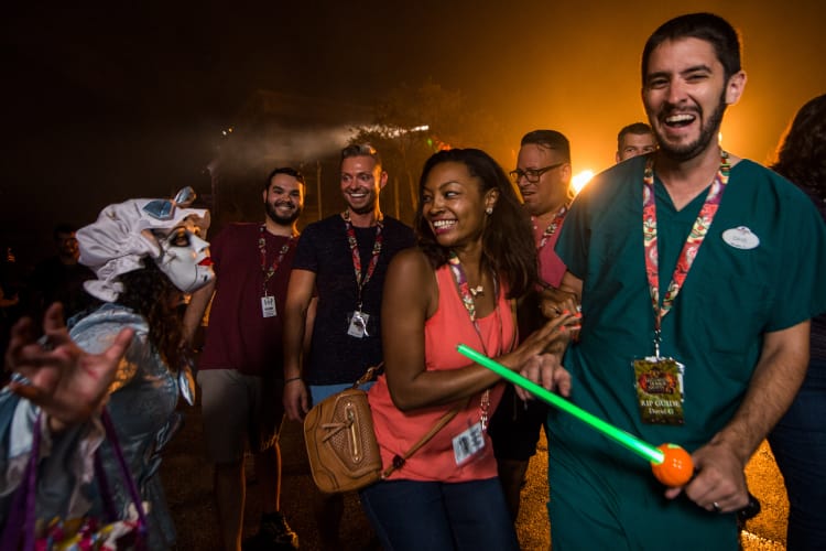 A scareactor with her face painted white leans towards smiling guests and a tour guide, all wearing R.I.P. Tour lanyards.