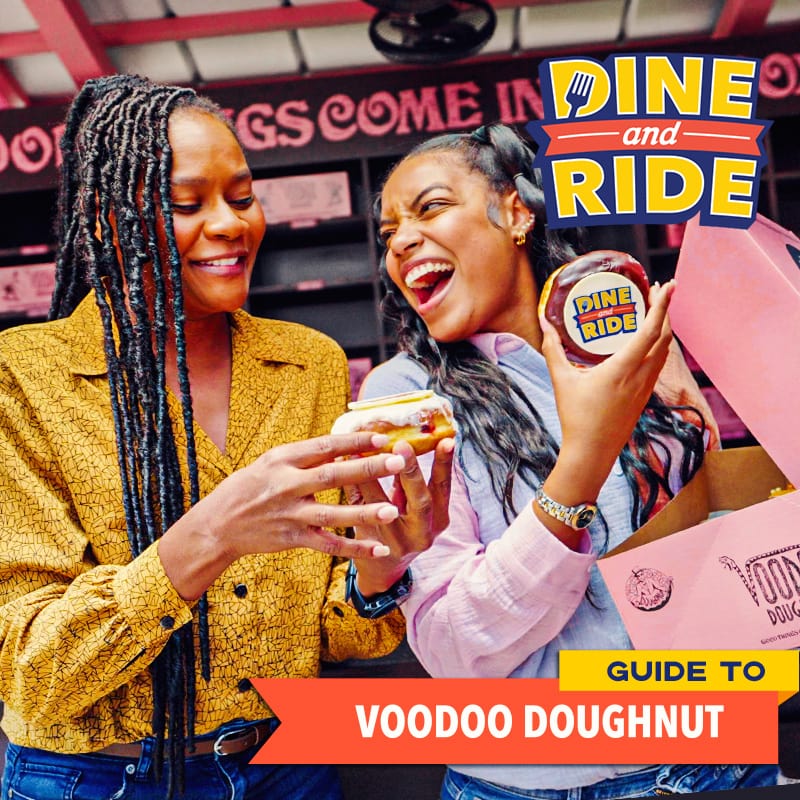 The Dine and Ride Hosts holding a pink box of VooDoo Doughnuts with the words ‘GUIDE TO VOODOO DOUGHNUT’ at the top right.