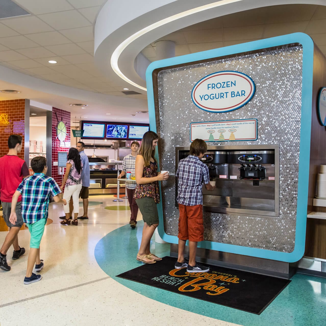 Visitantes caminan por el patio de comidas dentro del Bayliner Diner donde se encuentra yogur congelado, pizza y mucho más en Universal's Cabana Bay Beach Resort.