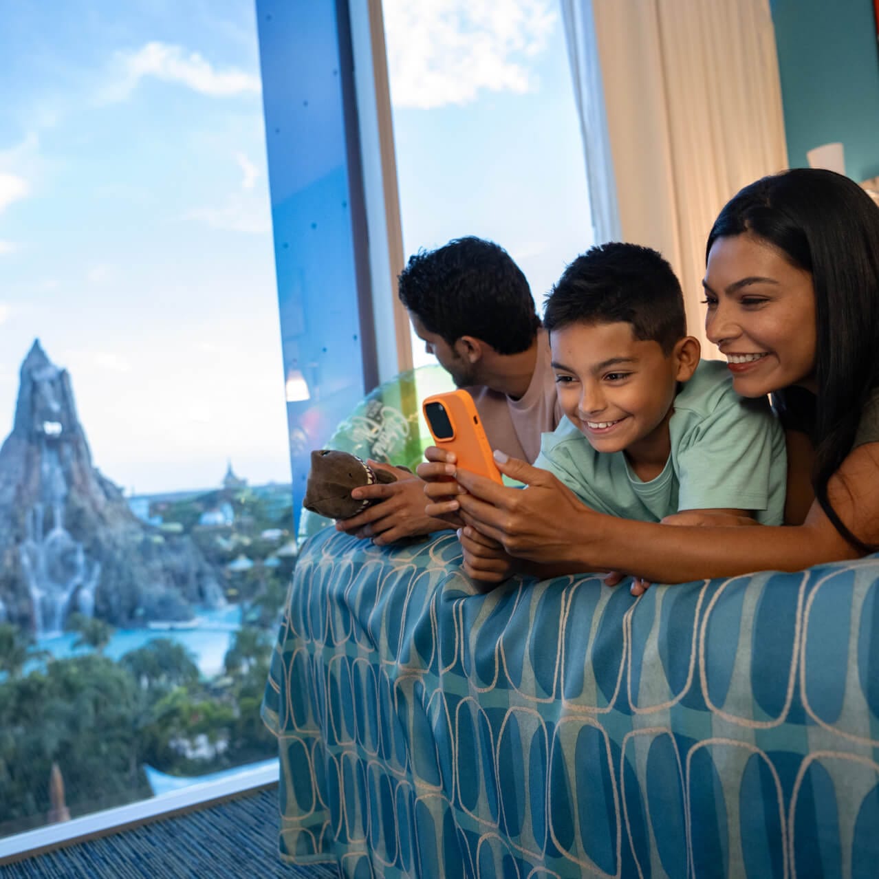 A happy family of three relaxing in their hotel room at Cabana Bay Beach Resort overlooking Volcano Bay.