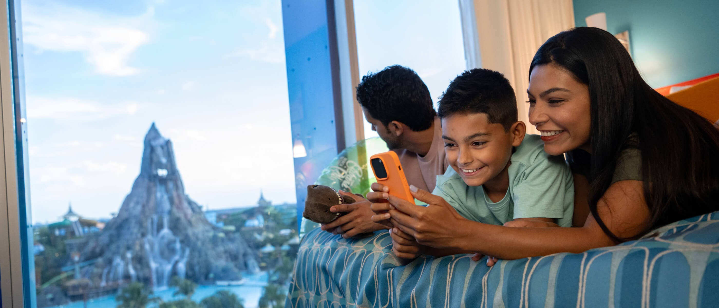 Una familia feliz de tres personas que se relajan en su habitación de hotel en Cabana Bay Beach Resort con vistas a Volcano Bay.