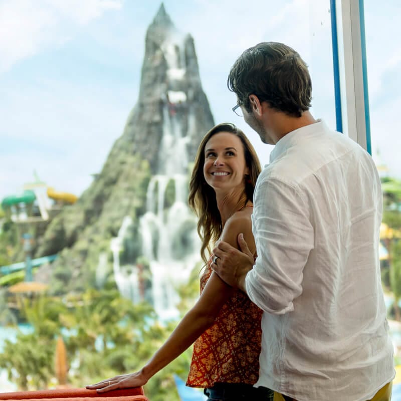 Una pareja mira hacia el parque acuático temático Universal Volcano Bay desde la ventana de un hotel de Universal.