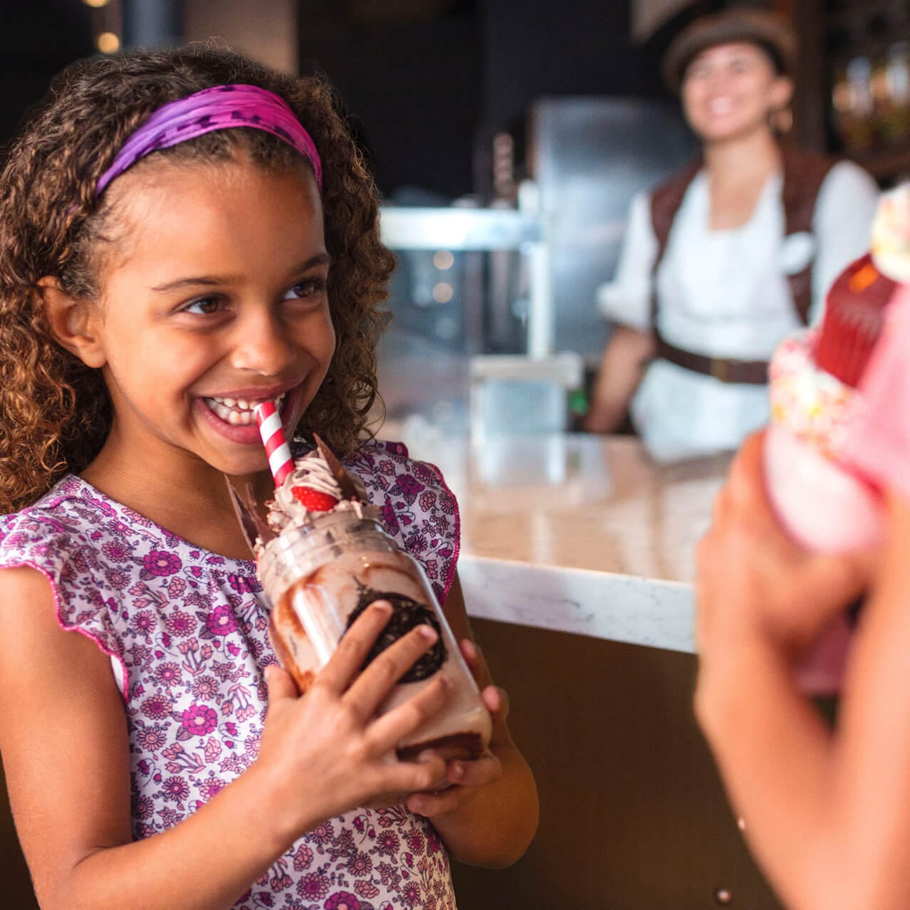 Una pequeña niña sonríe mientras bebe una batida deliciosa de chocolate, una de las especialidades de Toothsome Chocolate Emporium and Savory Feast Kitchen en Universal CityWalk Orlando.
