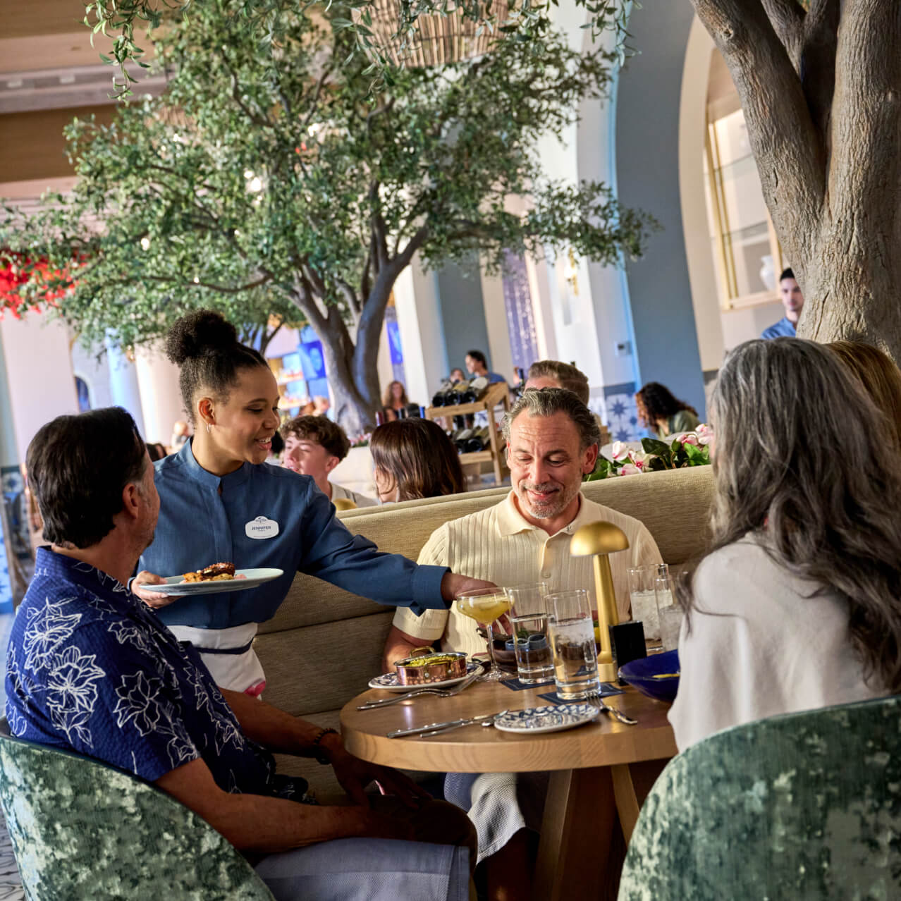 Una mesera lleva platos principales a los visitantes de Flora Taverna, dentro de Universal Helios Grand Hotel, a Loews Hotel
