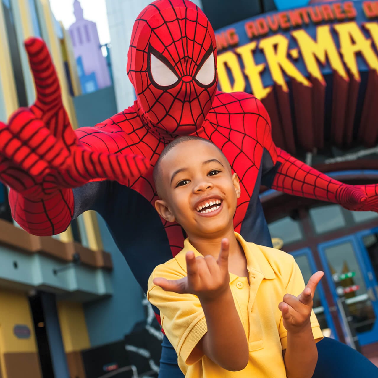 Un niño sonríe mientras posa junto a Spider Man afuera de la atracción The Amazing Adventures of Spider Man en Universal's Islands of Adventure Orlando.