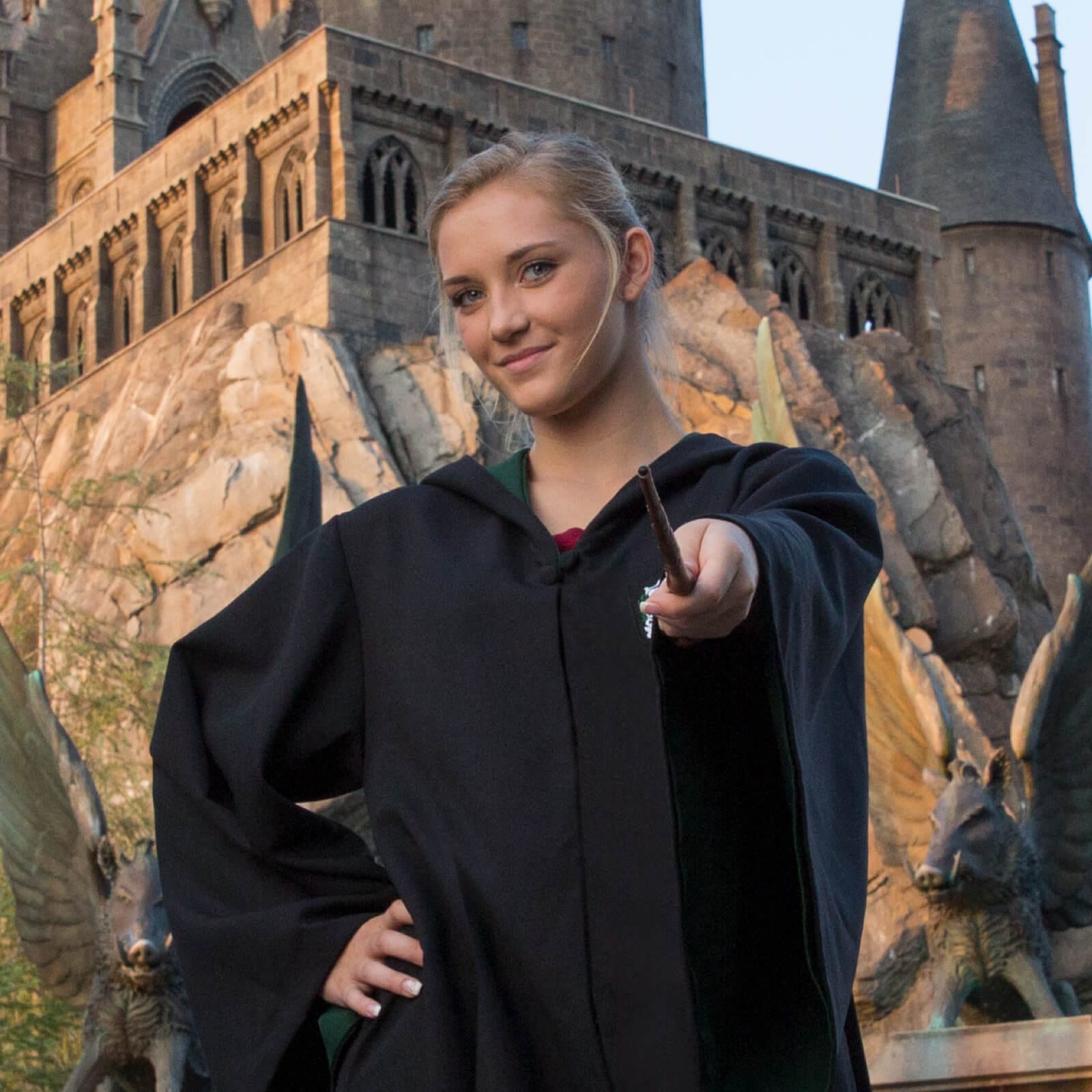 Niña con una capa de bruja sosteniendo una varita frente al castillo de Hogwarts™ en The Wizarding World of Harry Potter™ - Hogsmeade™.