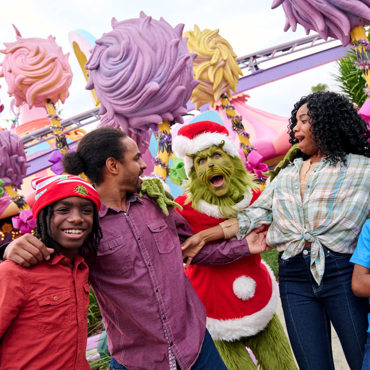 Cuatro personas posan con el Grinch vestido de Santa con Seuss Landing en el fondo.