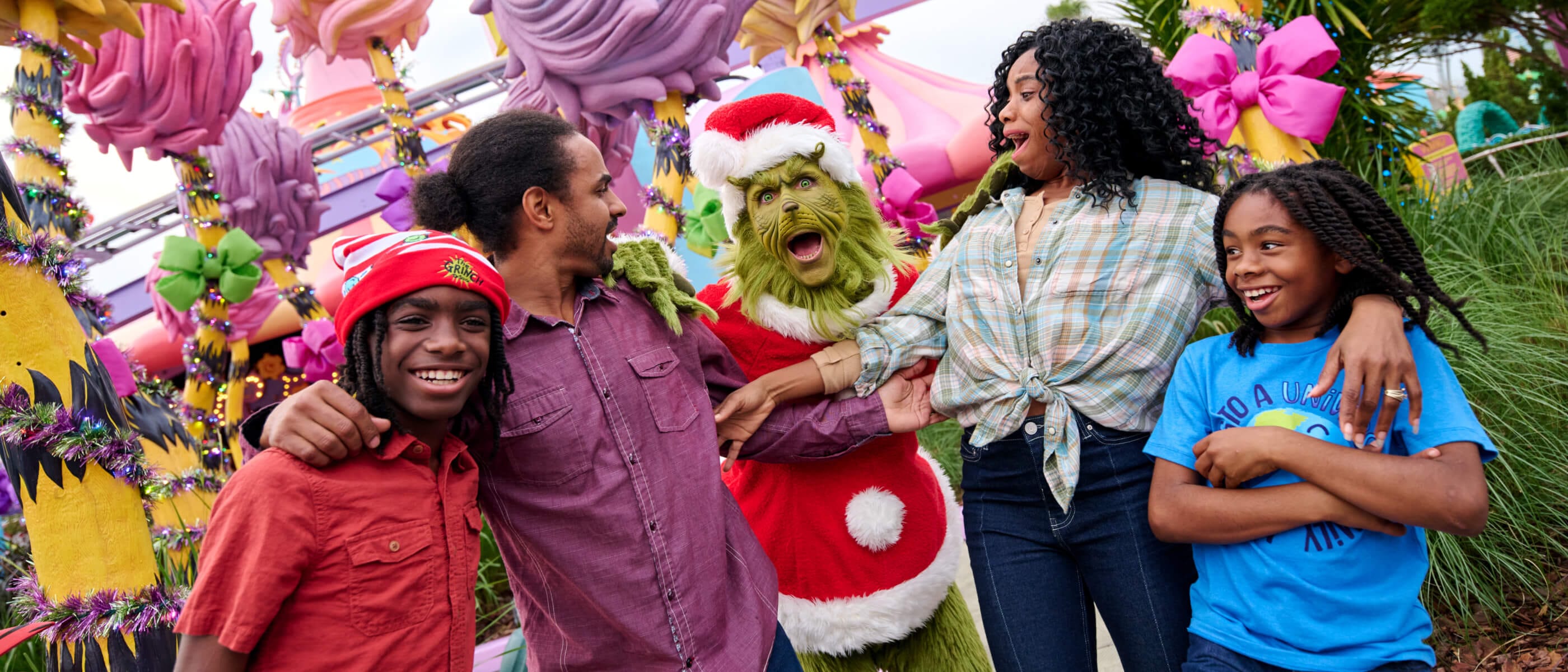 Cuatro personas posan con el Grinch vestido de Santa con Seuss Landing en el fondo.