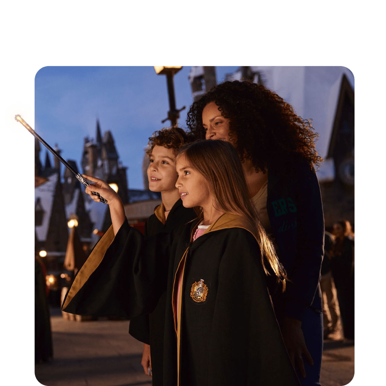 Una mamá con dos niños exploran The Wizarding World of Harry Potter™ - Hogsmeade™ con su varita interactiva de segunda generación.