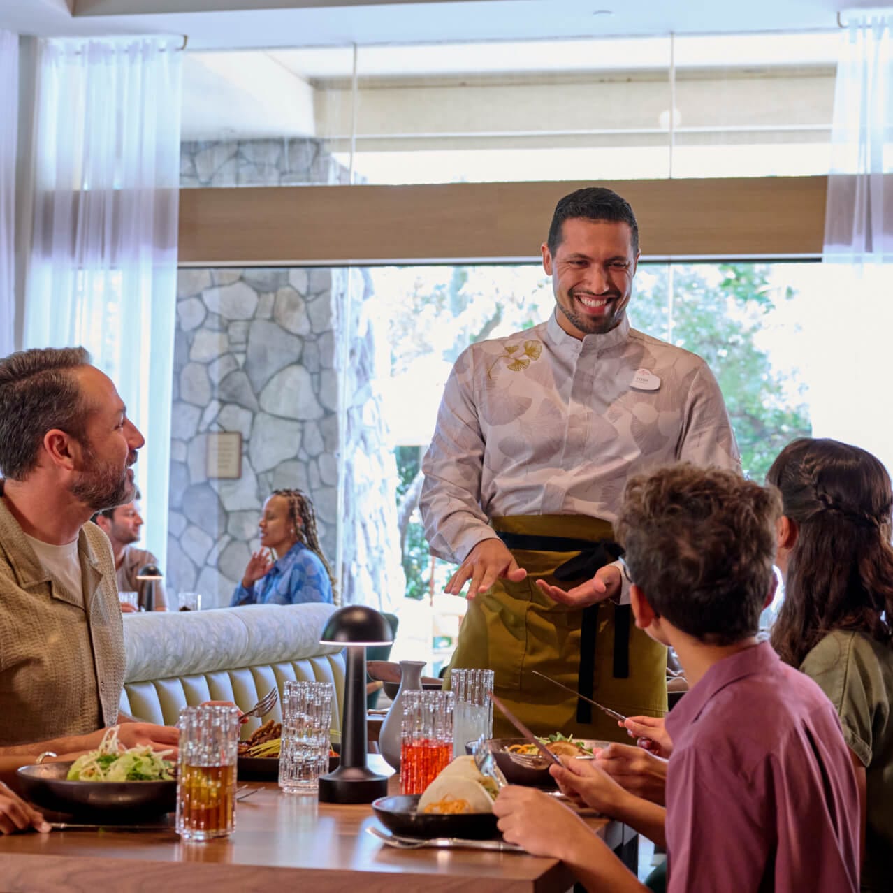 Un camarero habla con una familia en Islands Dining Room en Loews Royal Pacific Resort.