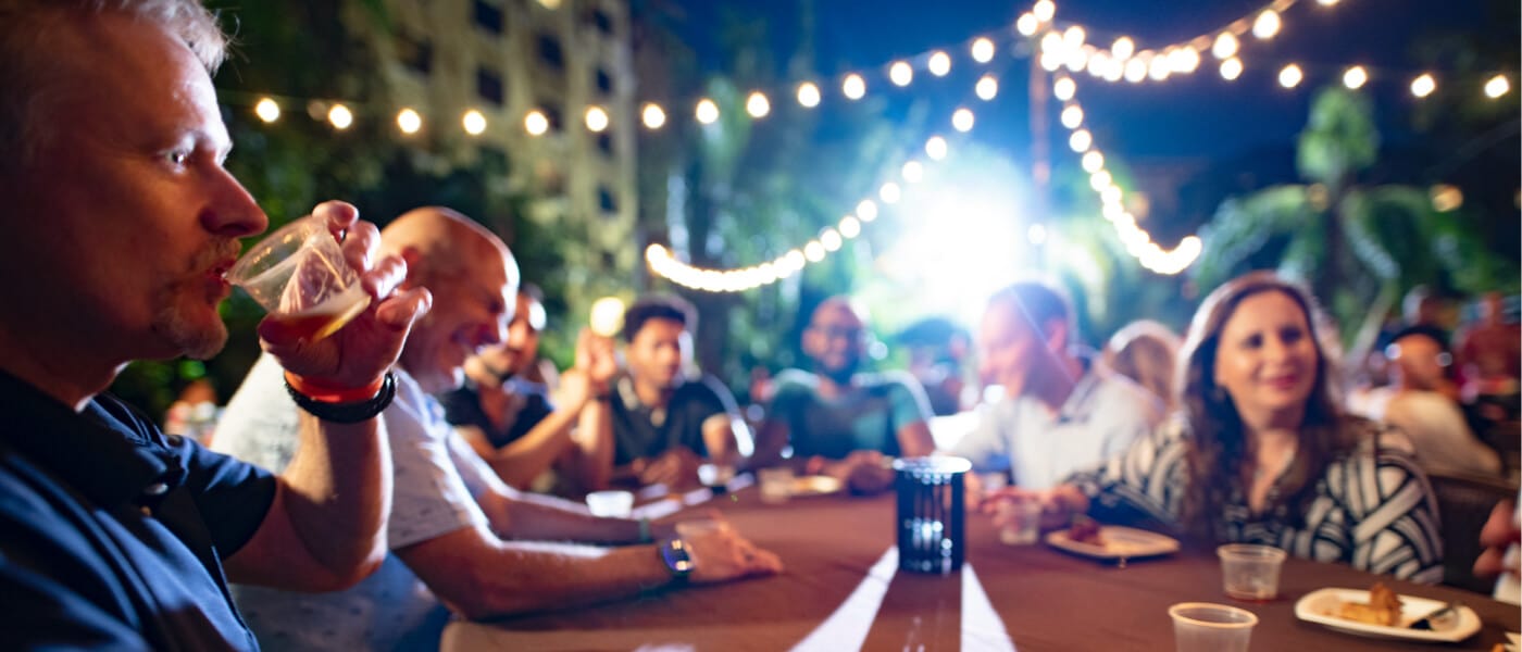 Un grupo de adultos sentados a una mesa de café en cómodas sillas de estilo isleño en el Jake's American Bar, un prestigioso restaurante y bar del Loews Royal Pacific Resort en Universal Orlando.