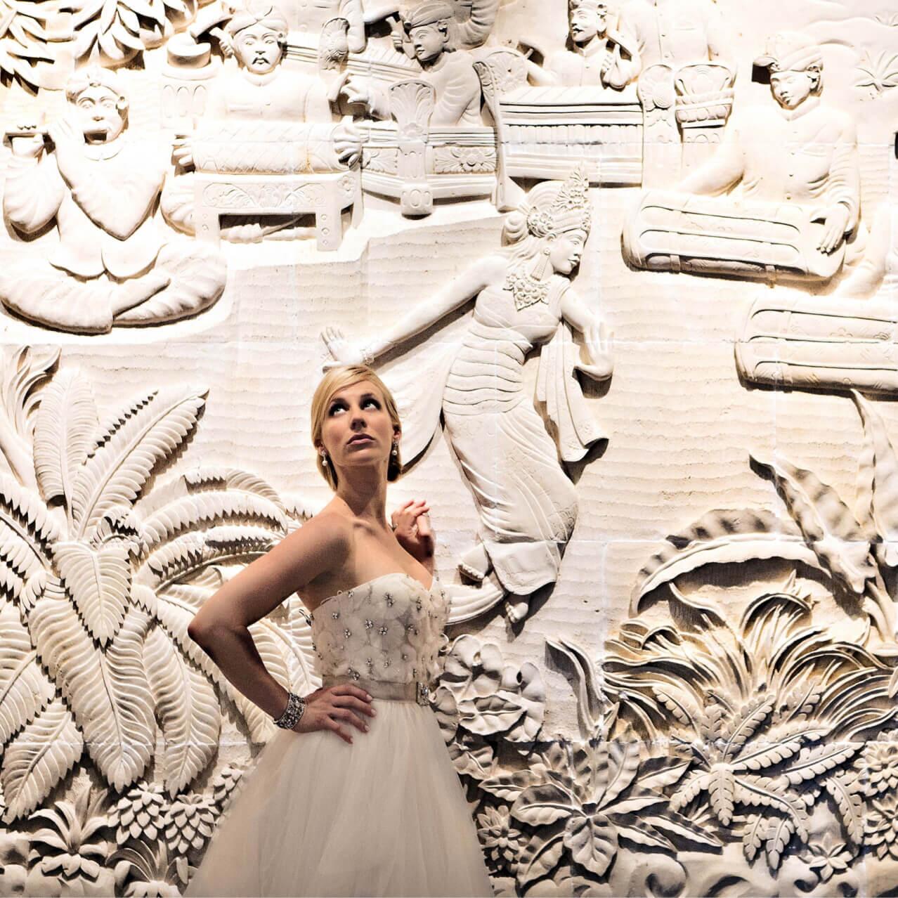 Una novia posa con la mano en la cintura frente a un gran mural tallado en el Loews Royal Pacific Resort, en Universal Orlando.