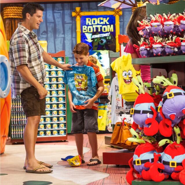 Un padre y su hijo admiran una camiseta azul brillante de Bob Esponja en SpongeBob StorePants de Universal Orlando.
