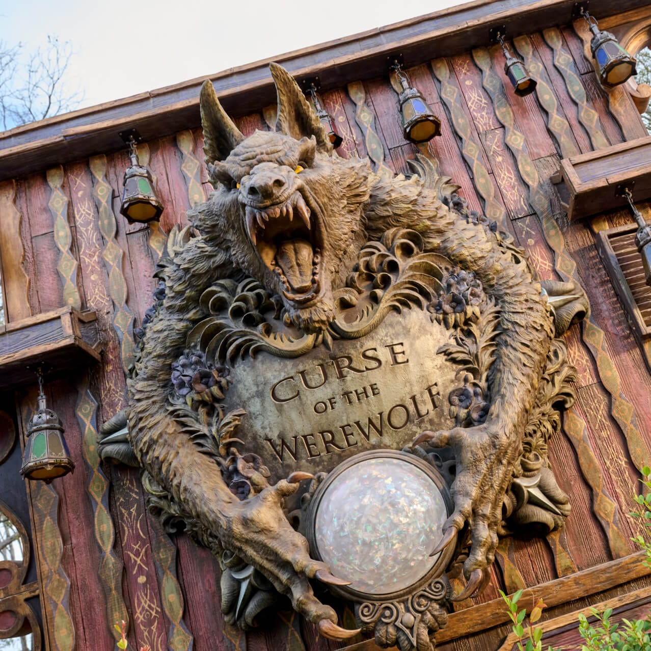 Fachada exterior de Curse of the Werewolf, con una gran escultura de hombre lobo con ojos amarillos mostrando sus colmillos y sosteniendo un medallón parecido a una piedra de luna con el nombre de la atracción grabado.