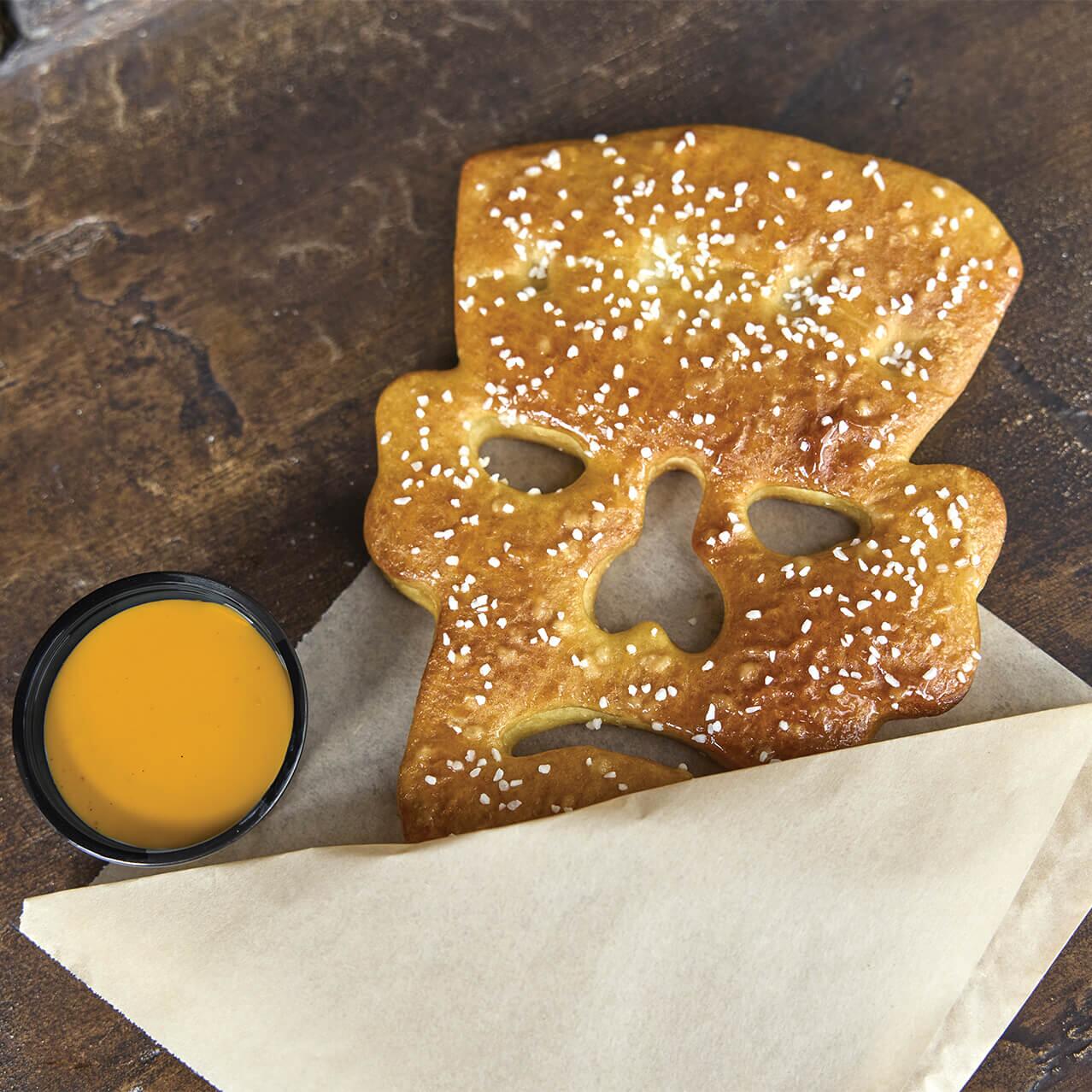 Un pretzel de Frank & Friends con la forma de la cabeza del monstruo de Frankenstein, con una porción de queso al lado.