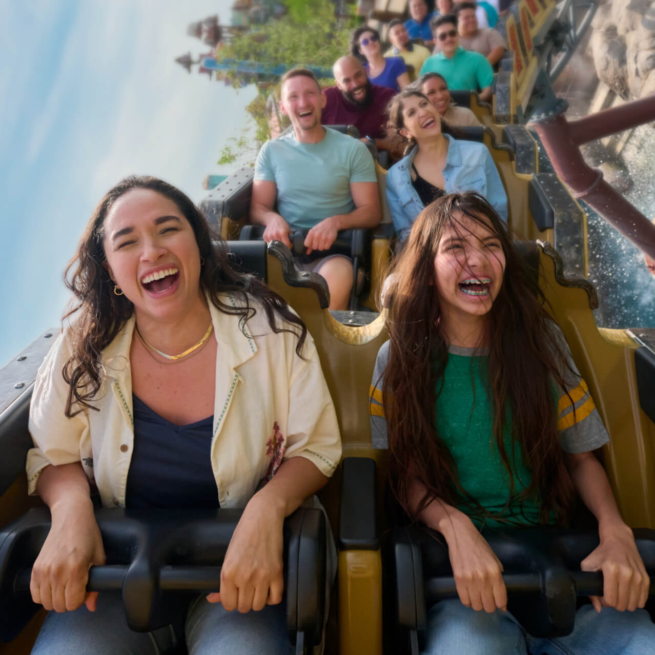 A mother and daughter laughing as their roller coaster vehicle soars through a sideways turn over the water.