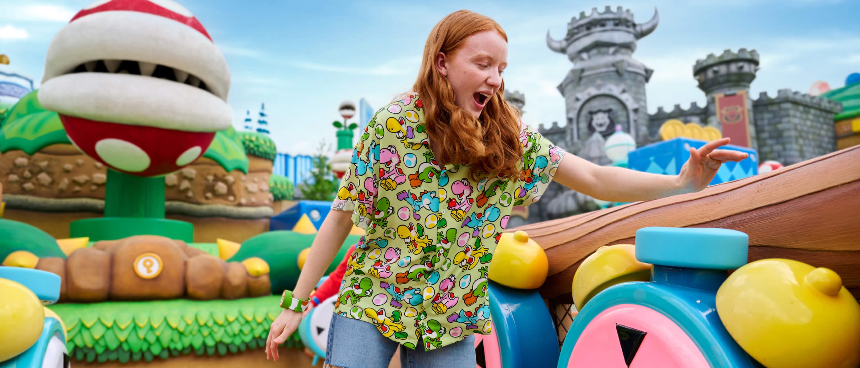 Un Visitante emocionado con una Power-Up Band™ verde tocando un reloj enorme en el colorido SUPER NINTENDO WORLD™.
