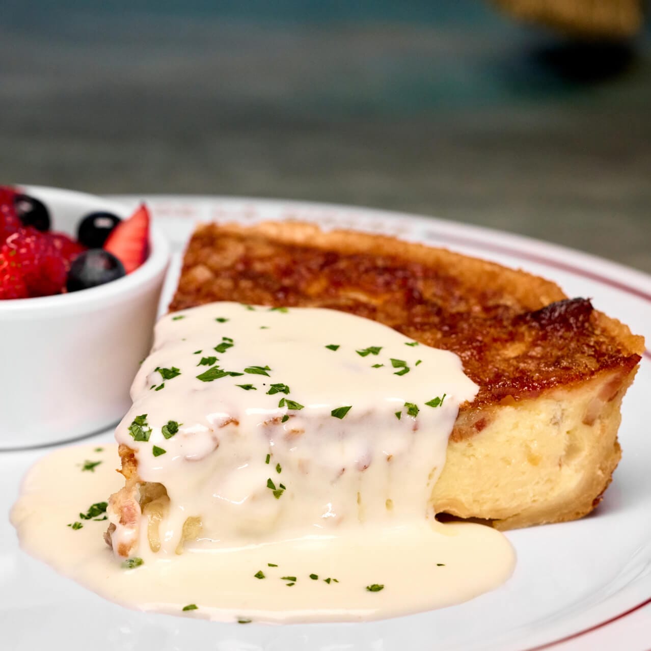 A savory dish of Quiche Lorraine with a side of fruit, served at Cafe L'air De La Sirene in The Wizarding World of Harry Potter™ — Ministry of Magic™.