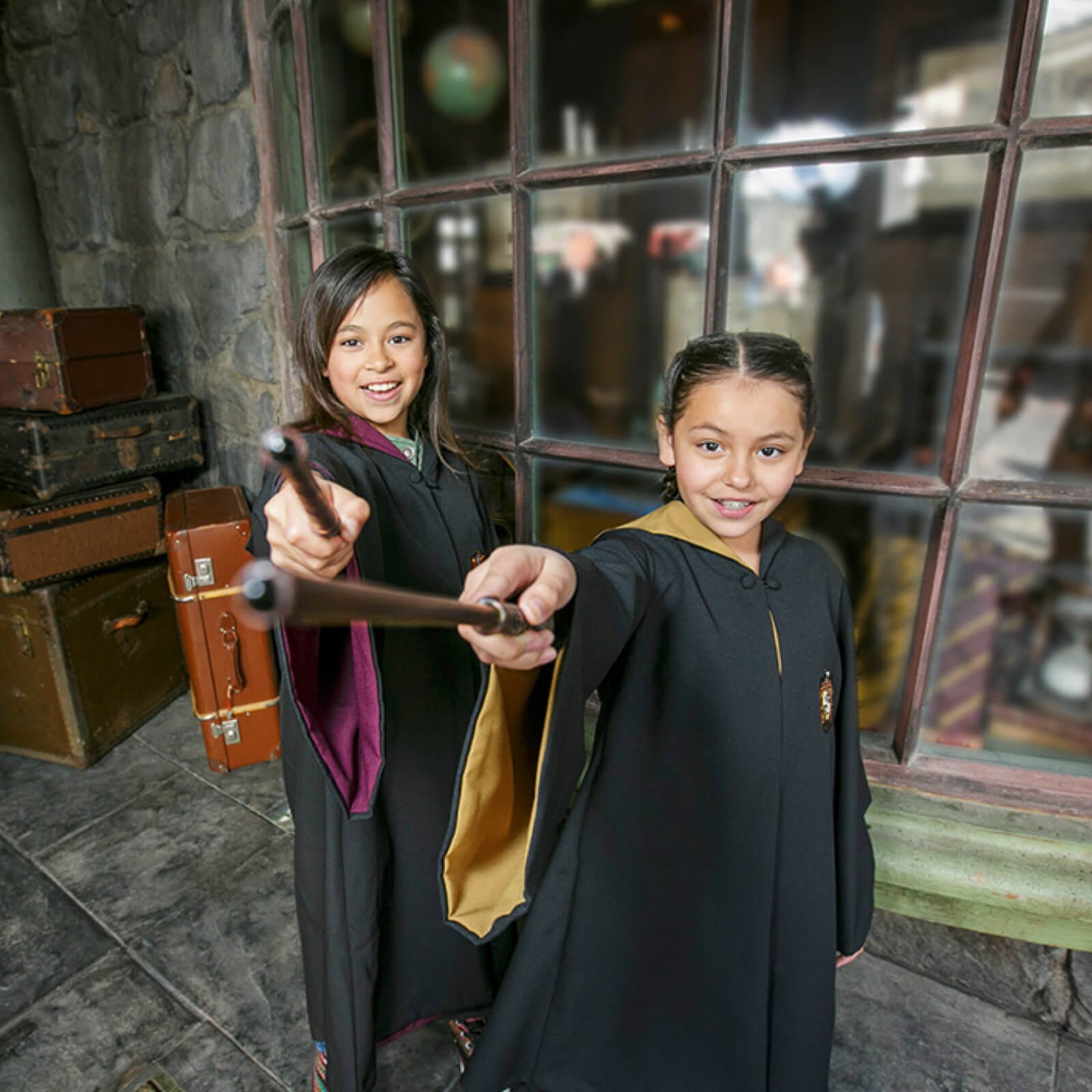Dos niñas con sus capas de Hogwarts™, sosteniendo varitas mientras intentan lanzar un hechizo.