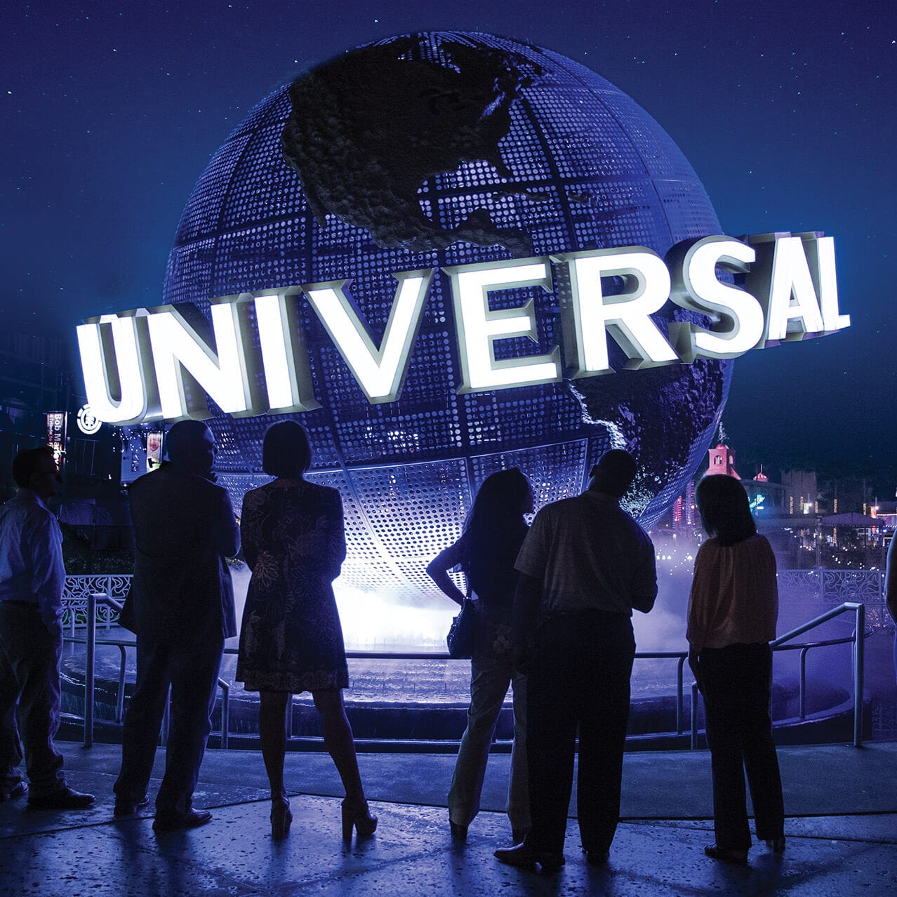 Seis asistentes contemplan el letrero iluminado del Globo de Universal durante la noche en Universal Orlando Resort.