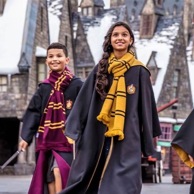 Dos niños con capas de Hogwarts™ caminando por las calles nevadas de Hogsmeade™.