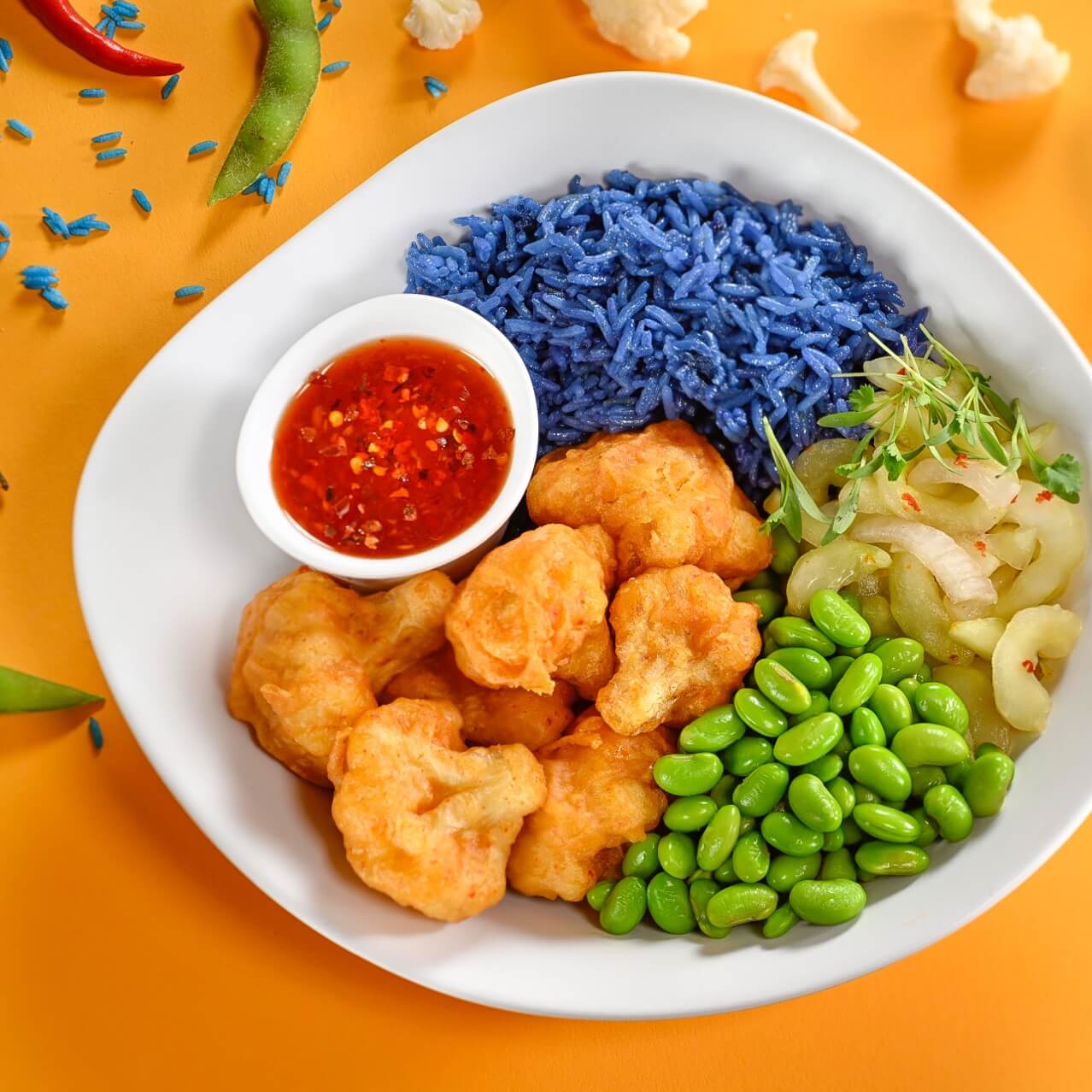 La Carl's Crispy Cauliflower sobre un fondo amarillo con algunos chiles y pepinillos esparcidos alrededor del plato.