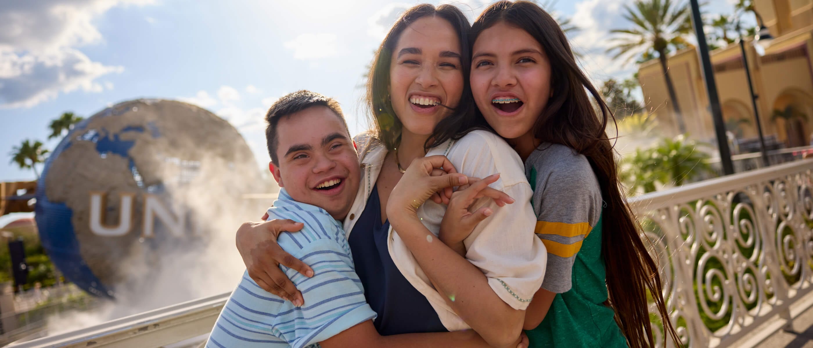 A family of three smiling and embracing as they pose for a photo together in front of the iconic Universal globe.