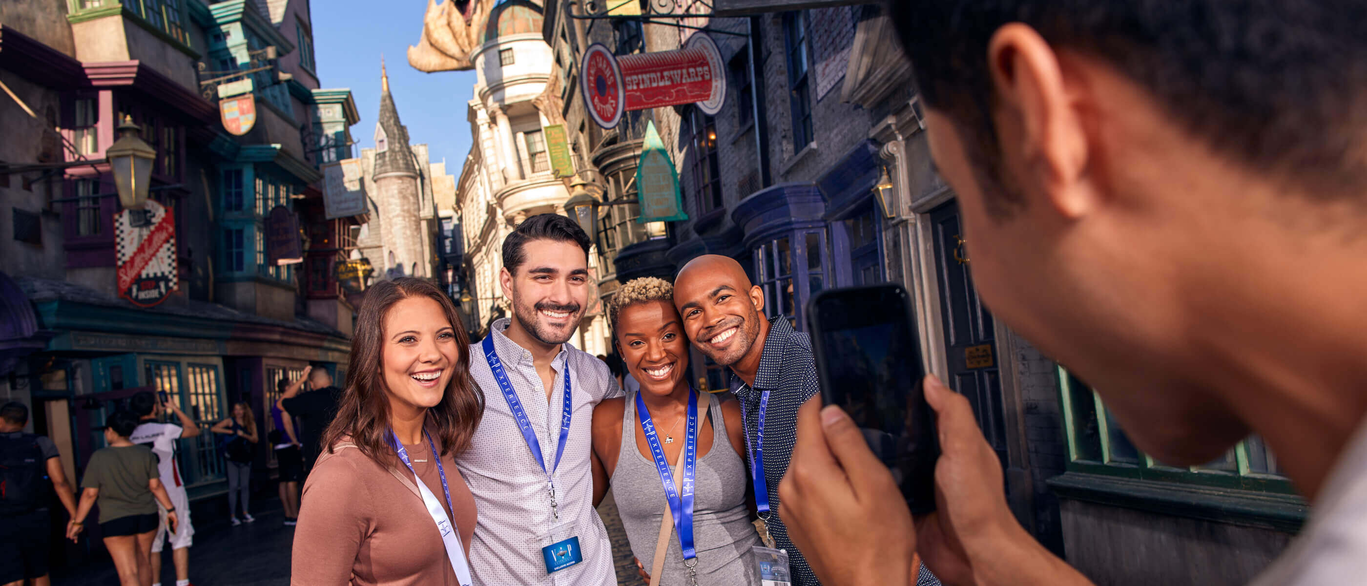 Cuatro visitantes sonrientes, con cordones identificativos, posan para una foto en el Diagon Alley™ con el dragón del banco Gringotts™ al fondo.