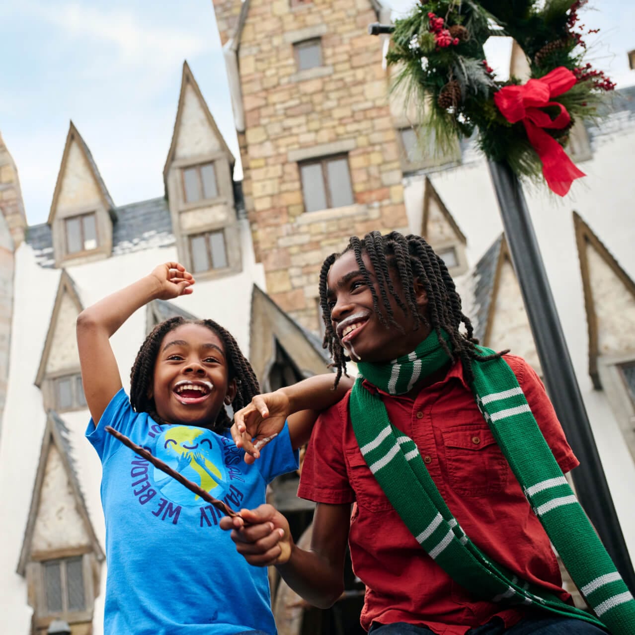 Dos personas con bigotes de Butterbeer™ jugando con una varita en Hogsmeade en™ The Wizarding World of Harry Potter™.