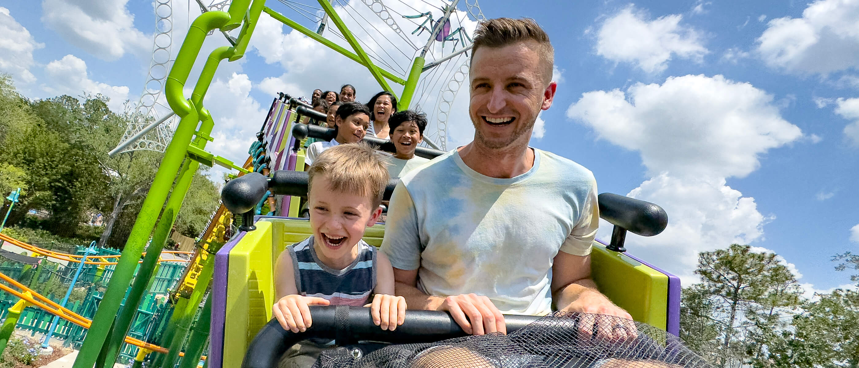 Un padre y un hijo sonríen y se ríen mientras montan en la montaña rusa Trolls de DreamWorks Land en Universal Studios Florida.
