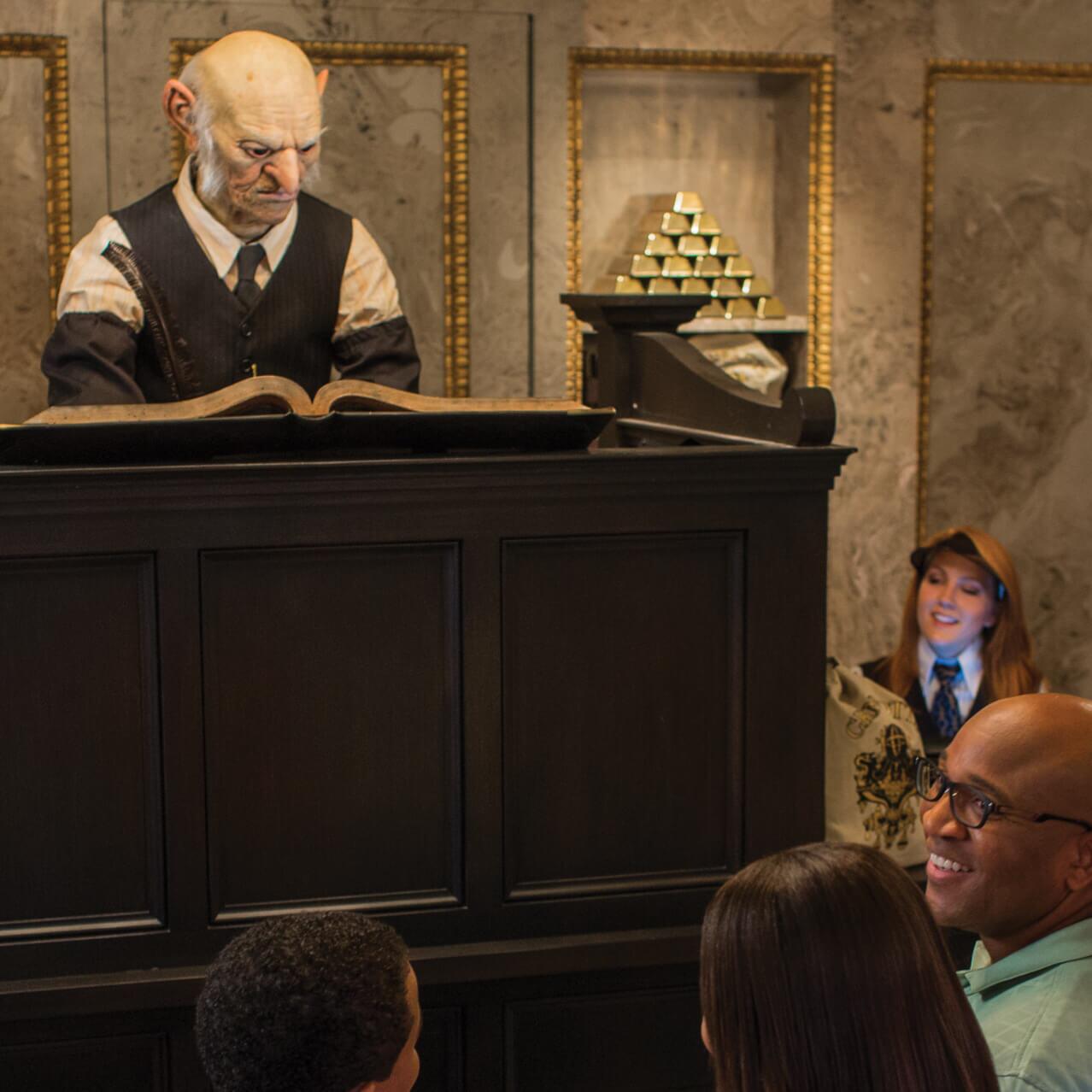 Una integrante del equipo de Gringotts Money Exchange le ayuda a un Muggle intercambiar sus monedas por dinero mágico dentro de Gringotts Money Exchange de Diagon Alley en The Wizarding World of Harry Potter de Universal Studios Orlando.